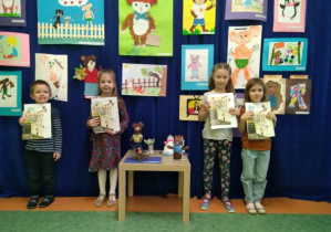 Dzieci z grupy Pszczółek pozują z nagrodami książkowymi za udział w konkursie na tle prac konkursowych.